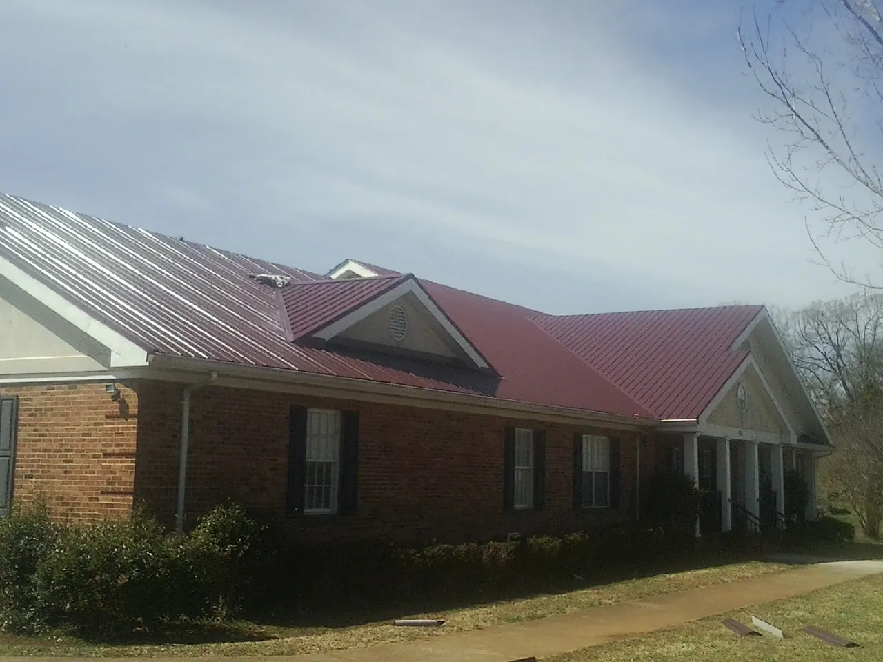 Red metal roof with gabled entries on a long brick building, from a Hail Damage Roof Repair job in Berwyn