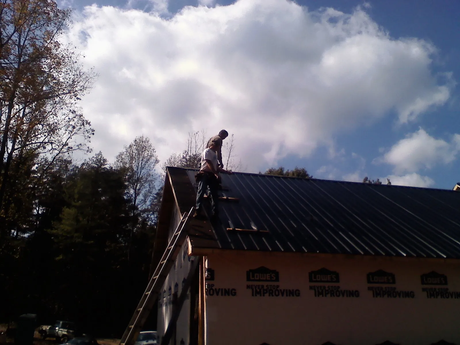 Roofer fastening dark metal panels high against a cloudy sky, from a Roof Inspection job in Berwyn
