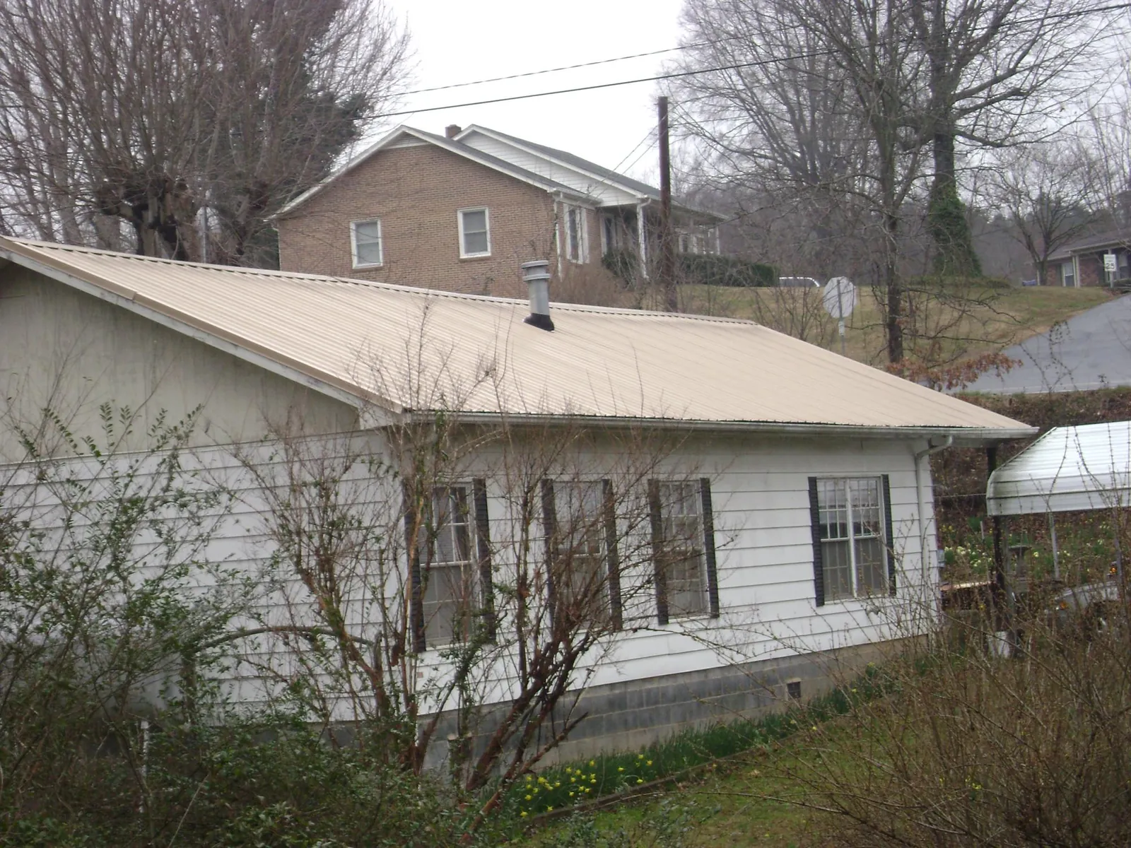 Tan metal roof on a white sided house set into a hillside — Commercial Roofing by Roofing Brothers in Berwyn